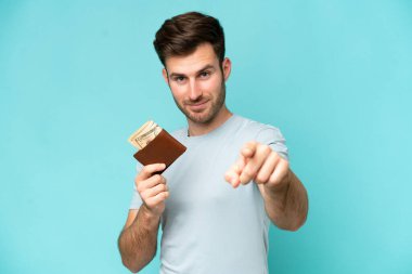 Mavi arka planda cüzdan tutan genç beyaz adam kendine güvenen bir ifadeyle sana işaret ediyor.