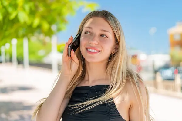Νεαρή Ξανθιά Γυναίκα Στο Ύπαιθρο Κρατώντας Μια Συνομιλία Κινητό Τηλέφωνο — Φωτογραφία Αρχείου