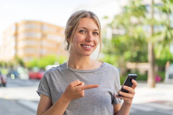 Young Blonde Woman Outdoors Using Mobile Phone Pointing — Stock Photo, Image