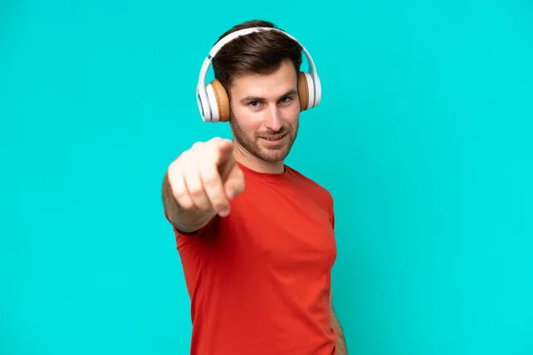Молодий Кавказький Чоловік Ізольований Синьому Фоні Слухаючи Музику Вказуючи Фронт — стокове фото
