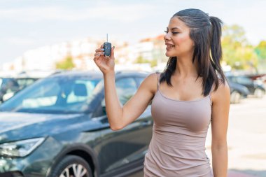 Dışarıda arabanın anahtarlarını tutan genç ve güzel bir kadın. Mutlu bir ifadeyle.