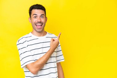 Izole sarı arka plan üzerinde genç yakışıklı adam şaşırttı ve tarafı işaret
