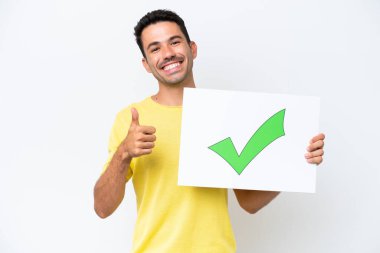 İzole edilmiş beyaz arka planda genç yakışıklı bir adam. Elinde yeşil işaret simgesi olan bir pankart var. Başparmağı yukarıda.