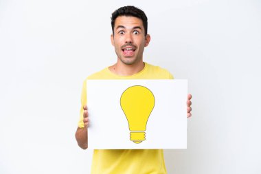 İzole edilmiş beyaz arka plan üzerinde genç yakışıklı bir adam elinde mutlu ifadeli bir ampul simgesi olan bir levha tutuyor.
