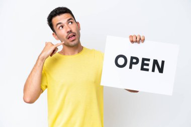 İzole edilmiş beyaz arka planda genç yakışıklı bir adam. Elinde açık yazılı bir pankart tutuyor ve telefon hareketi yapıyor.