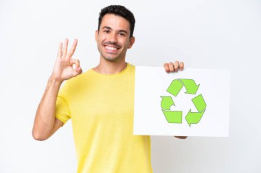 İzole edilmiş beyaz arka planda genç yakışıklı bir adam elinde geri dönüşüm simgesiyle bir pankart tutuyor ve zaferi kutluyor.