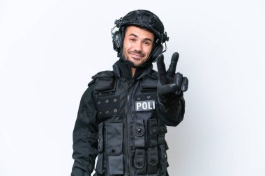 Beyaz arka planda izole edilmiş, gülümseyen ve zafer işareti gösteren Kafkasyalı genç bir SWAT askeri.