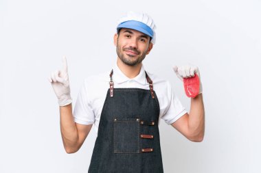 Kasap beyaz önlük giymiş ve izole edilmiş beyaz arka planda taze et servis ediyor ve en iyinin işareti olarak parmağını kaldırıyor.