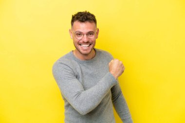 Sarı arka planda izole edilmiş beyaz yakışıklı bir adam zaferi kutluyor.