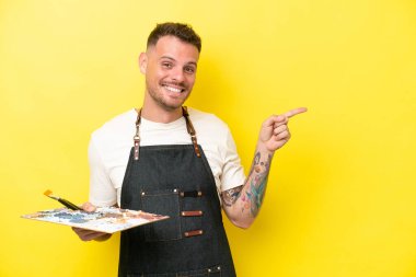 Sarı arka planda izole edilmiş bir palet tutan genç beyaz bir adam...