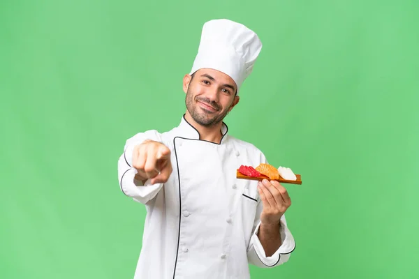 Young Caucasian Chef Holding Sushi Isolated Background Pointing Front Happy — Stock Photo, Image