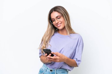 Genç Uruguaylı kadın beyaz arka planda izole edilmiş cep telefonuyla mesaj gönderiyor.