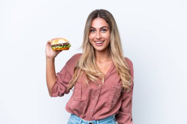 Genç, güzel Uruguaylı bir kadın elinde hamburgerle beyaz arka planda şaşırmış ve şok olmuş bir yüz ifadesi var.