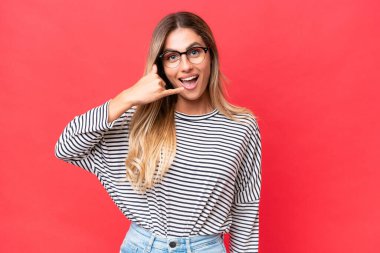 Genç Uruguaylı kadın, kırmızı arka planda izole edilmiş bir şekilde telefon jesti yapıyor. Bana geri dönüş işareti ver.