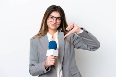 Beyaz arka planda izole edilmiş beyaz bir televizyon sunucusu olan genç beyaz kadın olumsuz bir ifadeyle baş parmağını aşağı gösteriyor.