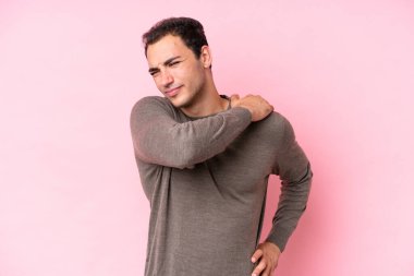 Genç, beyaz bir adam pembe arka planda izole edilmiş. Omuz ağrısı çekiyor. Çabaladığı için.