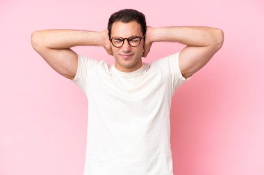 Pembe arka planda izole edilmiş genç beyaz adam hayal kırıklığına uğramış ve kulaklarını kapatmış.