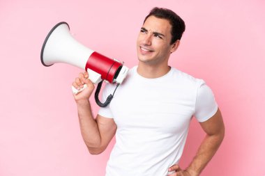 Pembe arka planda izole edilmiş genç bir beyaz adam elinde bir megafon ve düşünüyor.