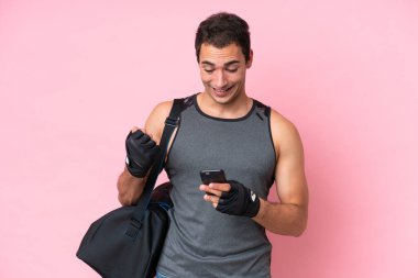 Young sport caucasian man with sport bag isolated on pink background surprised and sending a message