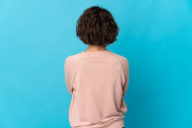 Young English woman isolated on blue background in back position
