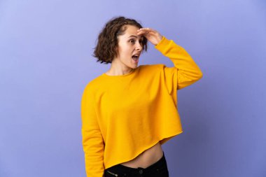 Mor arka planda izole edilmiş genç bir İngiliz kadın. Sürpriz bir ifadeyle yan tarafa bakıyor.