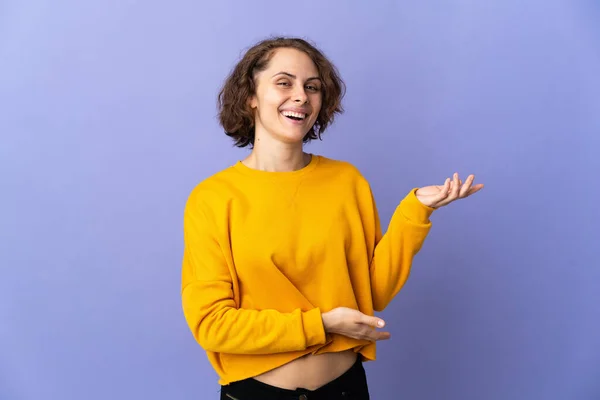 Young English woman isolated on purple background extending hands to the side for inviting to come