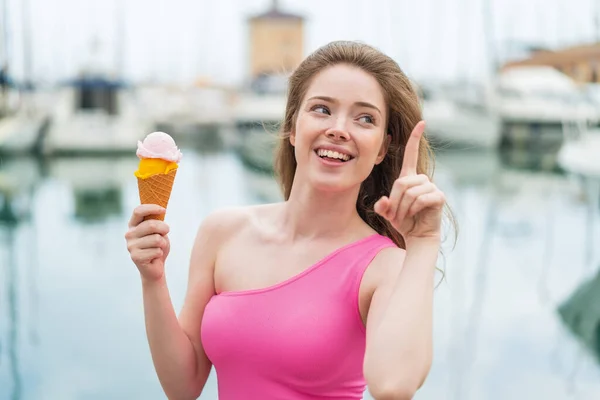 Young redhead woman with a cornet ice cream at outdoors intending to realizes the solution while lifting a finger up