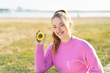 Genç ve güzel bir kız avakado tutuyor ve gülümsüyor.