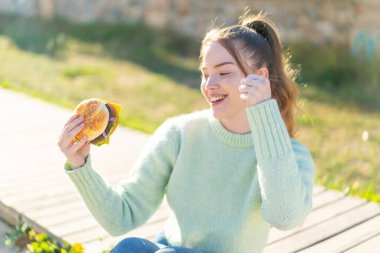 Dışarıda elinde hamburgerle genç güzel bir kız zaferi kutluyor.
