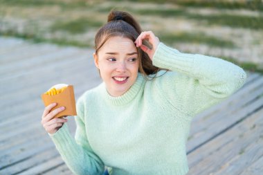 Genç ve güzel bir kız dışarıda patates kızartması tutuyor. Şüpheleri var ve kafası karışmış bir yüz ifadesi var.