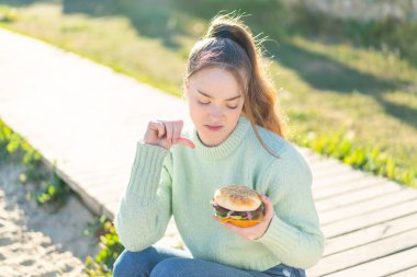 Genç ve güzel bir kız elinde hamburgerle dışarıda