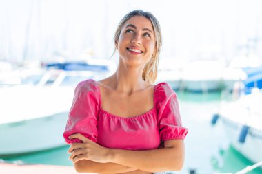 Açık havada genç sarışın bir kadın gülümserken yukarı bakıyor.