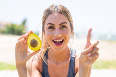 Avokado tutan genç sarışın kadın harika bir fikri işaret ediyor.