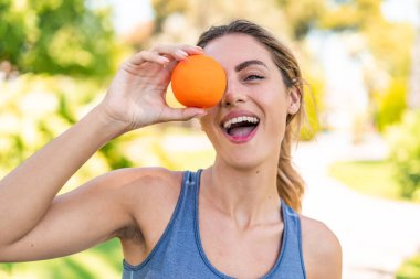 Açık havada genç sarışın bir kadın elinde turuncu bir suratla.