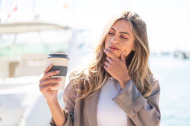 Güzel sarışın Uruguaylı kadın üzgün bir ifadeyle açık havada kahve tutuyor.