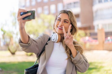 Genç, güzel sarışın Uruguaylı kadın dışarıda selfie çekiyor.