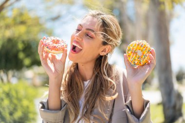 Genç, güzel sarışın Uruguaylı kadın açık havada elinde mutlu bir ifadeyle donut tutuyor.