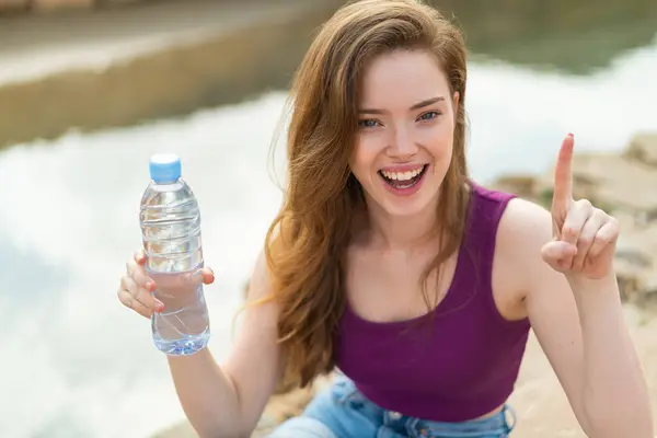 Jonge Roodharige Vrouw Met Een Fles Water Buiten Wijzend Een — Stockfoto