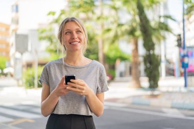 Açık havada cep telefonu kullanan genç sarışın bir kadın.