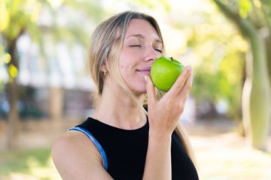 Açık havada, elinde elma tutan genç sarışın kadın.
