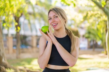 Açık havada, elinde elma tutan genç sarışın kadın.
