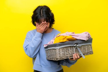 Arjantinli genç adam elinde çamaşır sepeti tutuyordu. Sarı arka planda, yorgun ve hasta bir ifadeyle izole edilmişti.