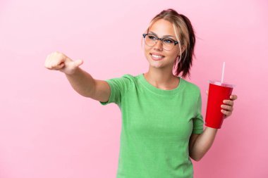 Pembe arka planda izole edilmiş serinletici bir şey tutan genç Rus kadın baş parmak işareti yapıyor.