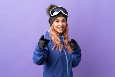 Snowboard gözlüklü kayakçı kız. Mor arka planda. Şaşırmış ve öne bakıyor.