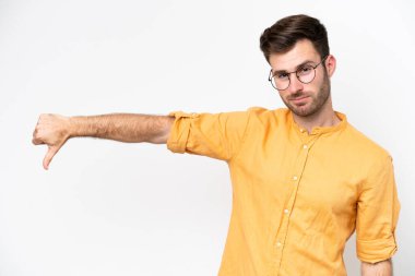Beyaz arka planda izole genç beyaz adam olumsuz ifade ile baş parmağını göstermektedir