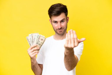 Kafkasyalı genç bir adam, sarı arka planda izole edilmiş bir sürü para alıyor. Bizimle gelmesi için davet ediliyor. Gelmene sevindim.