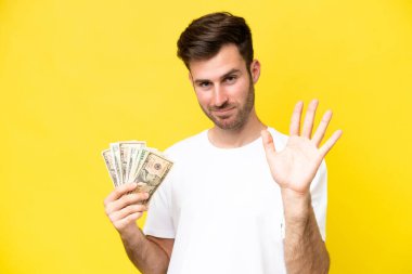 Kafkasyalı genç bir adam, sarı arka planda izole edilmiş bir sürü para alıyor mutlu bir ifadeyle selamlıyor.