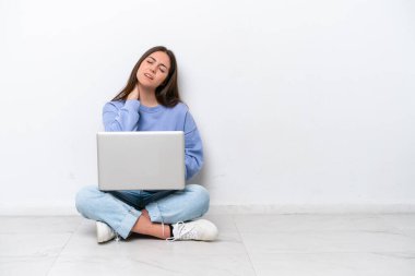 Dizüstü bilgisayarlı, beyaz arka planda boynu ağrıyan beyaz bir kadın yerde oturuyor.