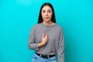 Mavi arka planda izole edilmiş genç beyaz kadın kendini işaret ediyor.