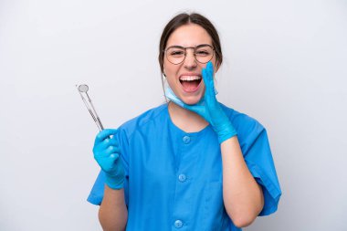 Beyaz arka planda izole edilmiş aletleri olan beyaz dişçi kadın ağzı açık bağırıyor.